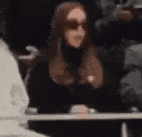 a woman wearing sunglasses and a black turtleneck is sitting at a table .