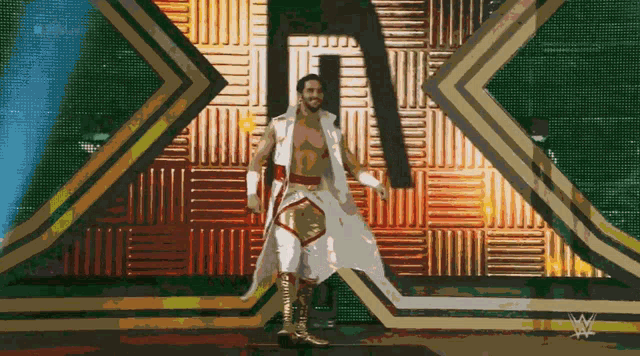 a man in a white and gold outfit is walking on a stage with a w logo in the background
