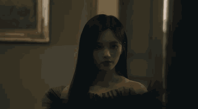 a woman in a black dress looks at the camera in a dark room