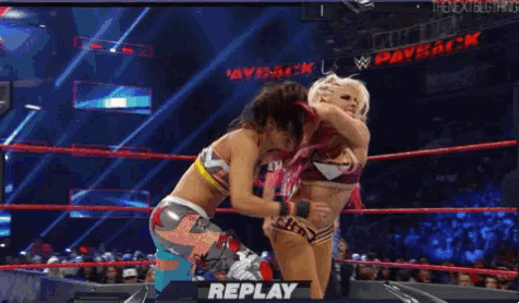 two women are wrestling in a wrestling ring with the words replay on the screen