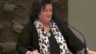 a woman wearing a leopard print scarf is speaking into a microphone while holding a pair of glasses