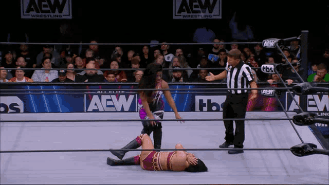 a woman is laying on the ground in a wrestling ring with aew wrestling advertisements behind her
