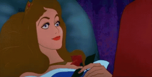 aurora from sleeping beauty is laying in bed holding a rose .