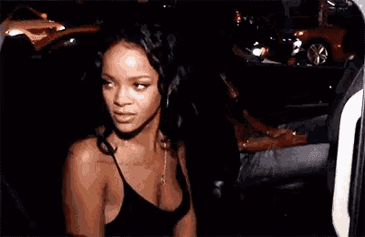 a woman in a black tank top is standing in a dark room with cars in the background .