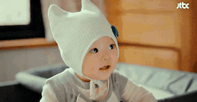 a baby is wearing a white hat with ears and a blue flower on it