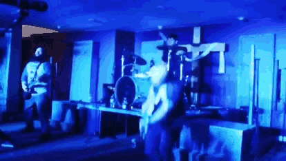 a man playing a guitar in a dark room with a cross on the wall