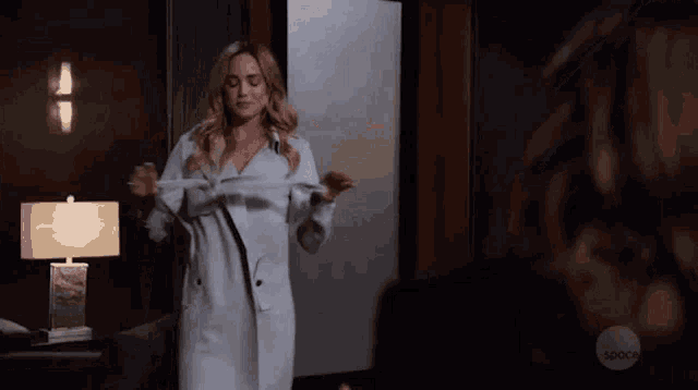 a woman in a white coat is standing in a room taking off her jacket .