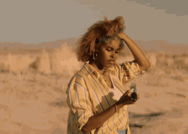 a woman in a striped shirt is standing in the desert holding a gun