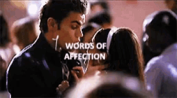 a man is kissing a woman on the cheek in front of a crowd with the words words of affection above them .