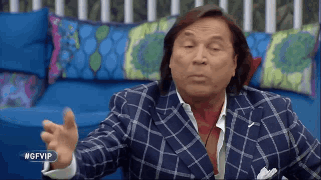 a man in a plaid suit is sitting on a blue couch with #gfvip written on the corner