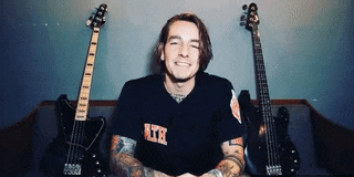 a man wearing a shirt that says rte is smiling in front of two guitars