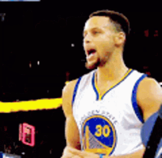 a basketball player wearing a golden state warriors jersey is standing on a court with his tongue out .