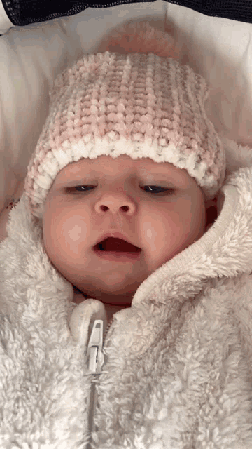 a baby wearing a pink and white knitted hat and a white jacket