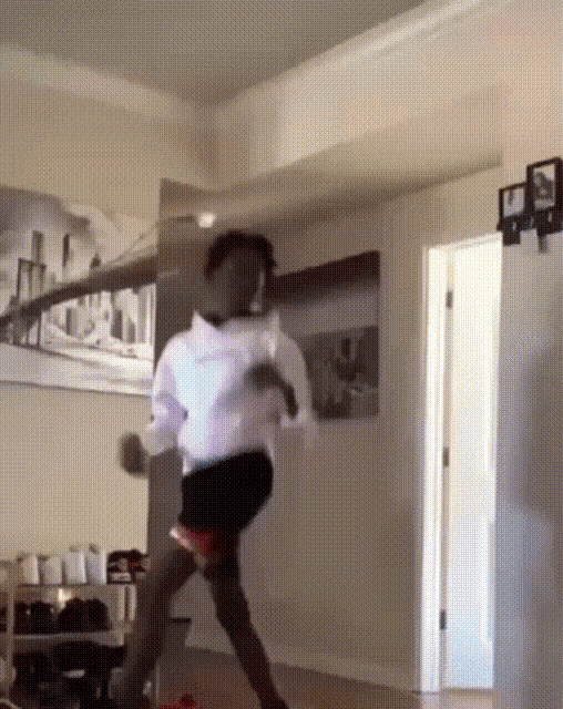 a person in a white shirt and black shorts is dancing in a room