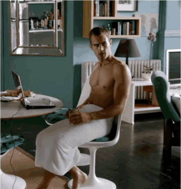 a shirtless man wrapped in a towel sits in a chair