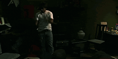 a man in a white shirt is dancing in a dark room in front of a tv