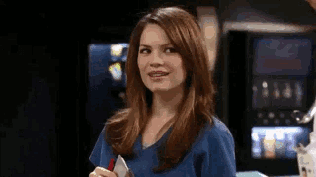a woman in a blue scrub top is smiling and holding a clipboard .