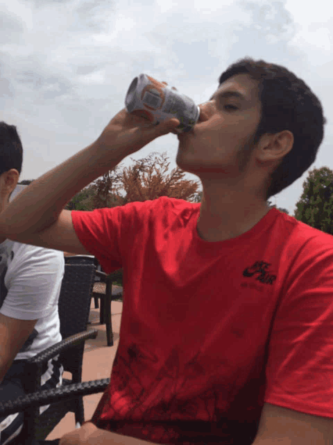 a young man in a red nike shirt drinks from a can