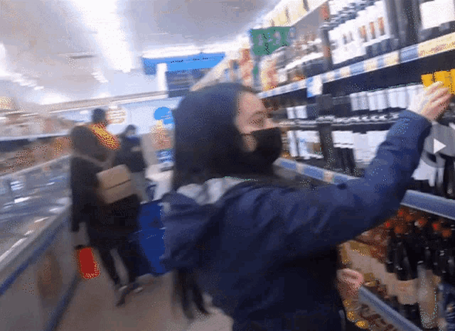 a woman wearing a black mask is looking at a bottle of wine