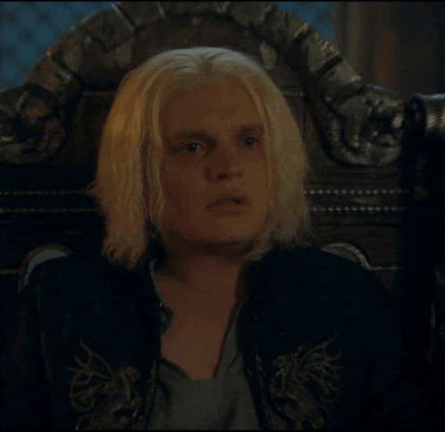 a man with blonde hair is sitting in a chair and looking at the camera