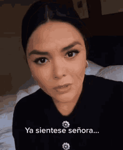 a woman is standing in front of a bed with a caption that says `` ya sientese señora '' .