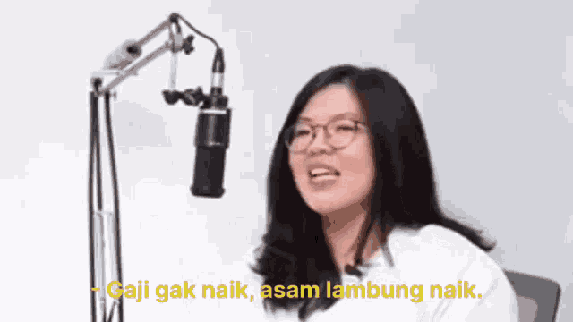 a woman wearing glasses is sitting in front of a microphone and talking .