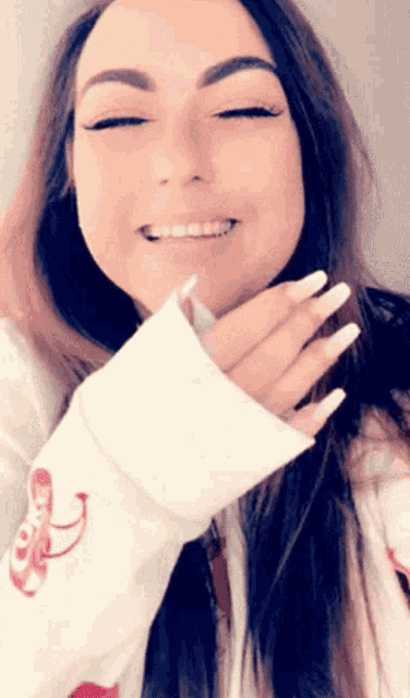 a woman with long white nails is smiling with her eyes closed and covering her mouth with her hand