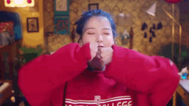 a woman with blue hair is wearing a red sweatshirt and making a face .