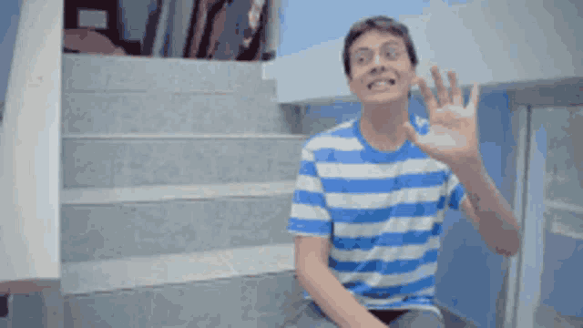a young man wearing a blue and white striped shirt is waving