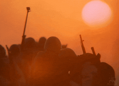 a group of soldiers are standing in front of a sunset and the sun is setting
