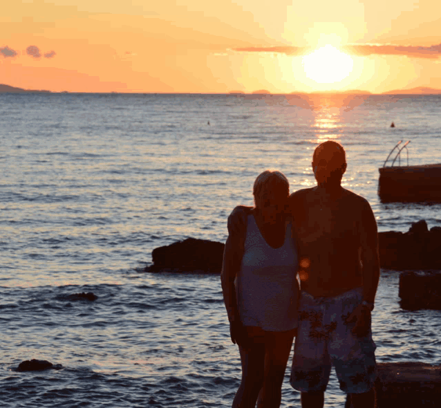 a man and a woman are posing for a picture in front of a sunset over the ocean