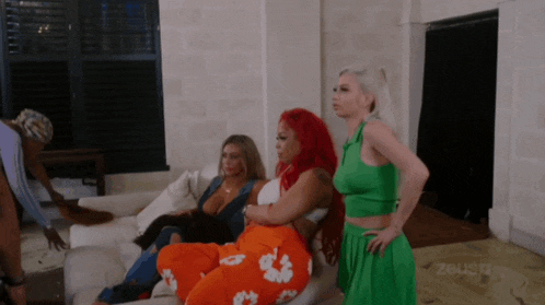 a group of women are sitting on a couch in a living room and one of them is wearing a green dress