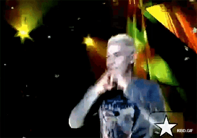 a man stands in front of a microphone with a rbd.gif star in the lower right corner