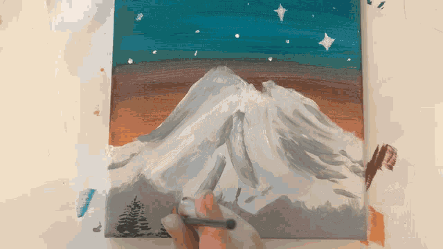a person is painting a mountain with a brush on a canvas