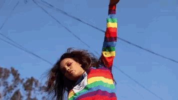 a girl in a rainbow striped shirt is reaching up into the air .