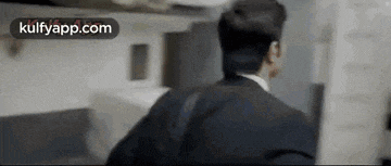 a man in a suit and tie is standing in a room and looking at something .