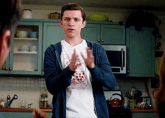 a young man wearing a hoodie and a t-shirt is clapping in a kitchen .