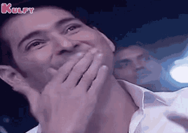 a man is covering his mouth with his hands while laughing .