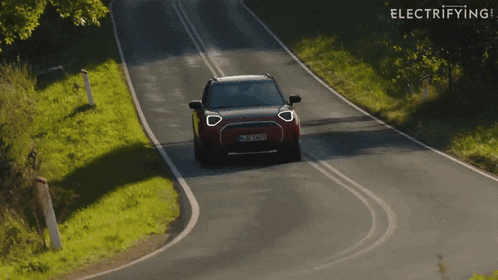 a red mini cooper driving down a road with the word electrifying in the background