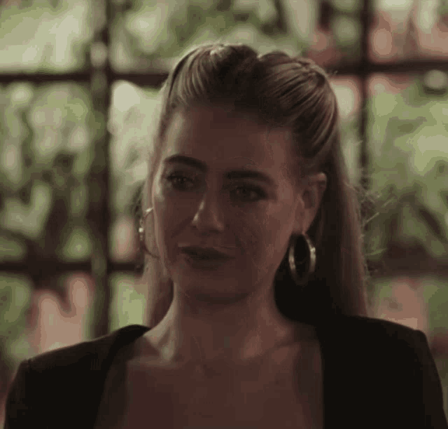 a woman wearing hoop earrings and a black jacket looks sad