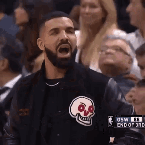 a man wearing a jacket with a skull on it is sitting in the stands during a basketball game .
