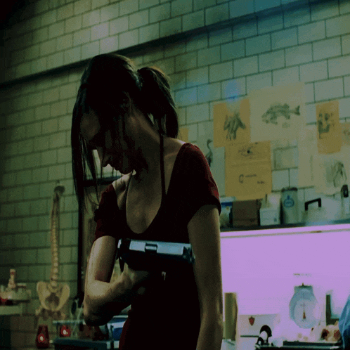 a woman in a red shirt is holding a gun in front of a wall with drawings of fish on it