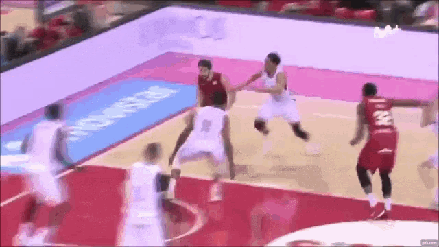 a group of basketball players are playing a game on a court with an ad for movistar in the background .