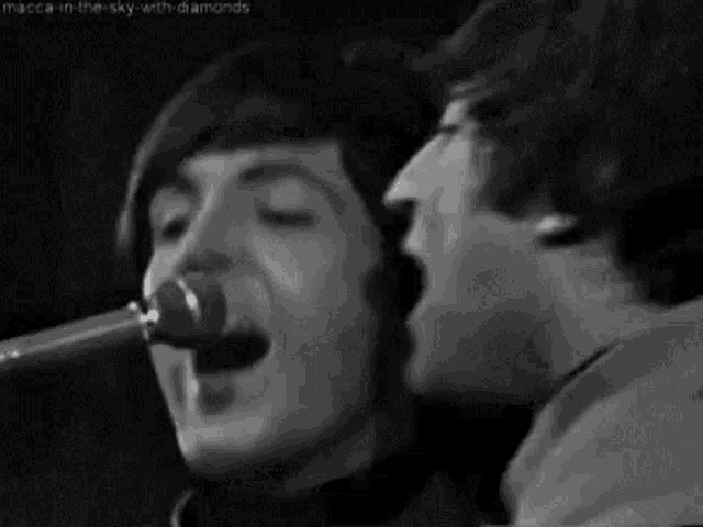 a man is singing into a microphone while another man looks on .