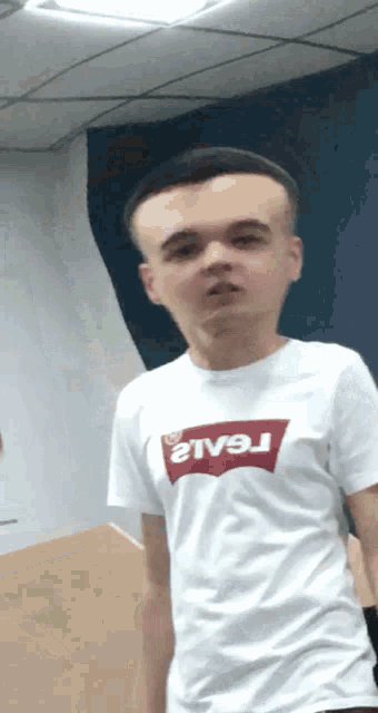 a young man wearing a white levi 's t-shirt looks at the camera