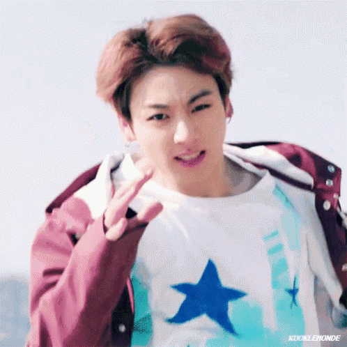 a young man wearing a white shirt with a blue star on it is giving a peace sign .