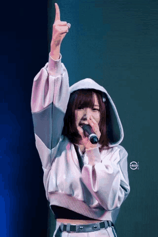 a girl in a hoodie is singing into a microphone with her hand in the air