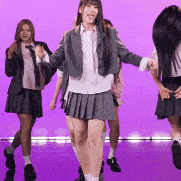 a group of girls in school uniforms are dancing on a purple stage