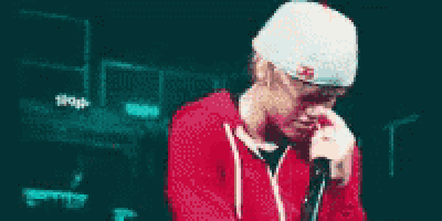 a man wearing a red hoodie and white hat is singing into a microphone .