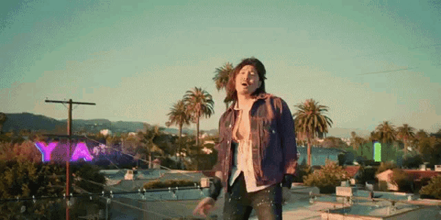a man in a denim jacket is standing on a rooftop in front of a sign that says ya
